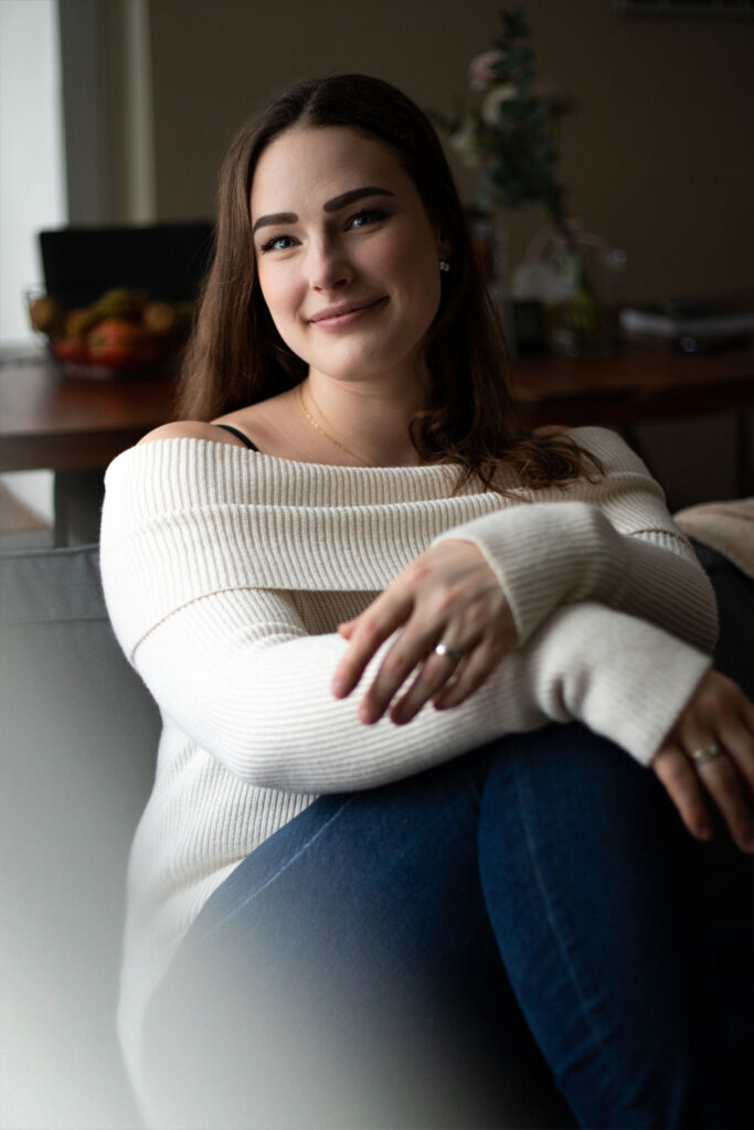 Naise portree. Istub diivanil, vaatab kaamerasse ja muigab.